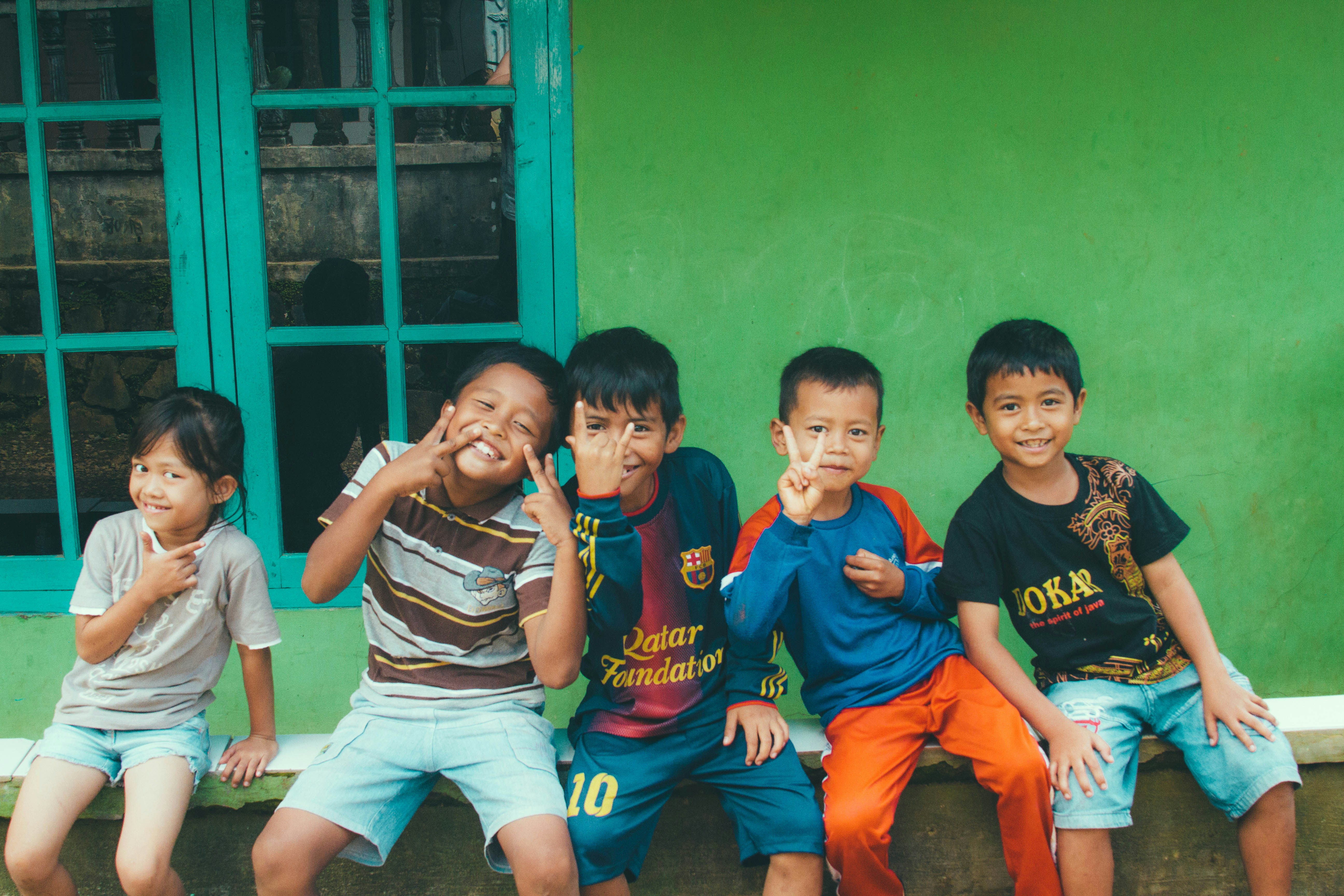 Children sitting on bench against green wall